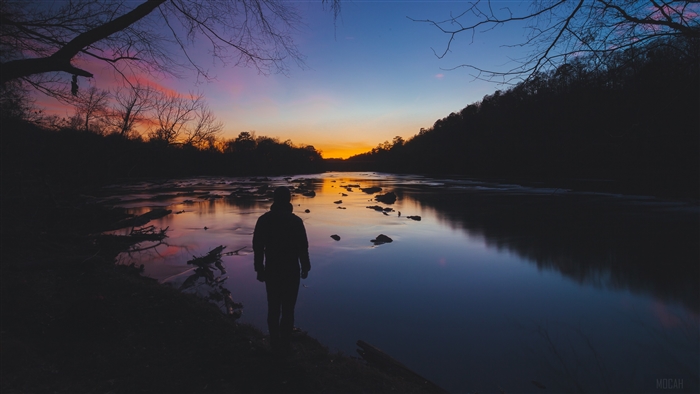 Man watching sunset over river with trees