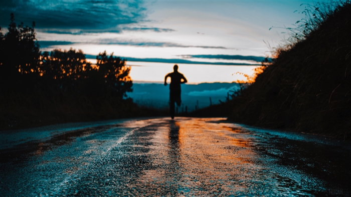 Silhouette of a person running on a wet asphalt road at sunset