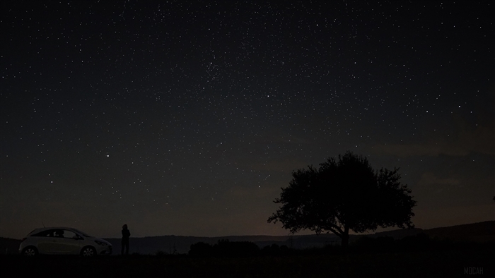 Starry night sky over a landscape with a tree and car