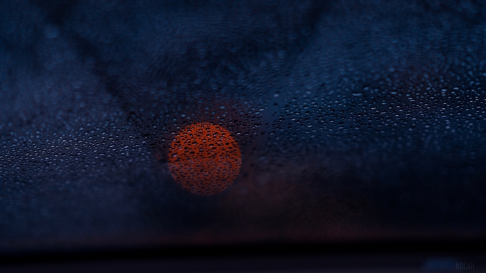 Close-up of water drops on glass with orange bokeh