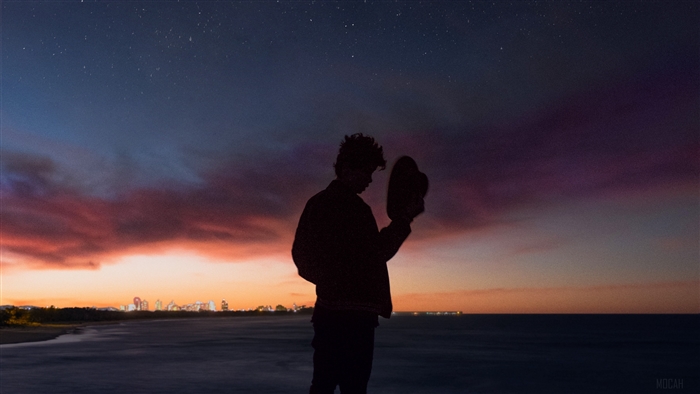 Silhouette of a person holding a hat against a starry sky and sunset