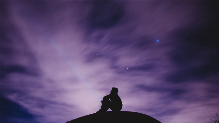 Silhouette of a person sitting on a hill under a starry purple sky