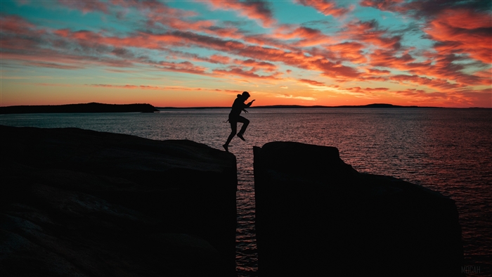 Silhouette of a person jumping over a sea chasm at sunset