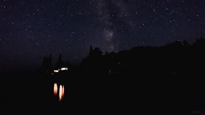 Starry night sky over a dark landscape with lights
