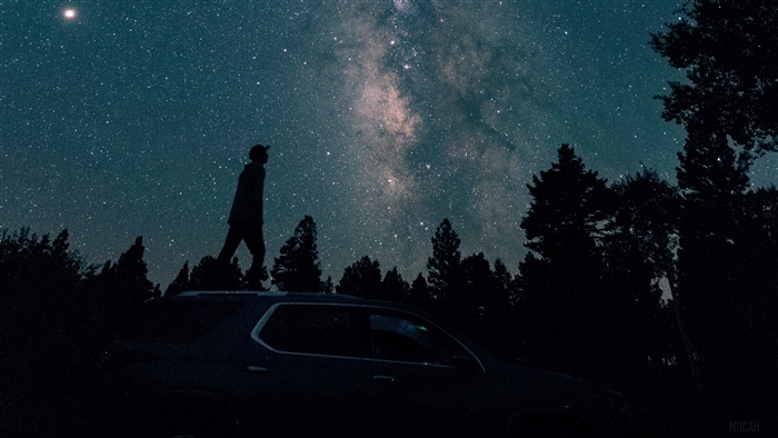 Silhouette of a person on a car under the Milky Way