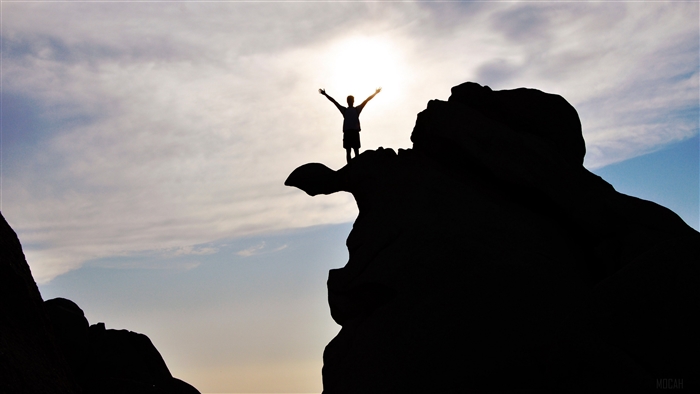 Silhouette of a person on a rock with arms raised