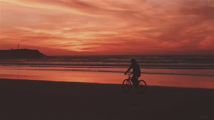 Bicyclist on beach at sunset 4K