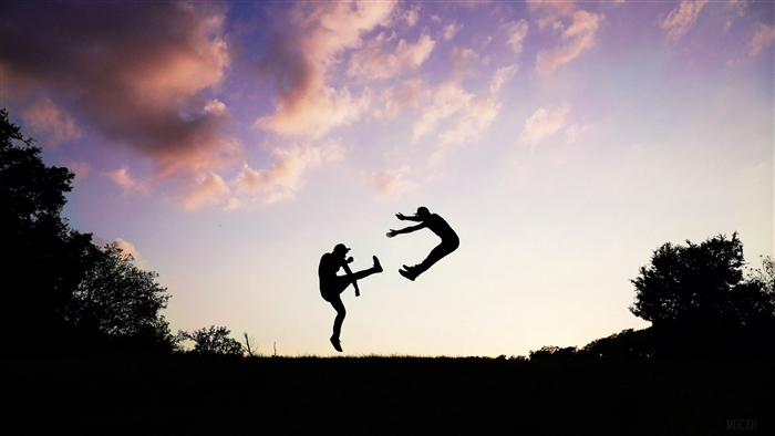 Two people silhouetted jumping against a sunset sky