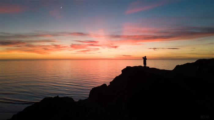 Silhouette of a person on a cliff overlooking the sea at sunset 4K
