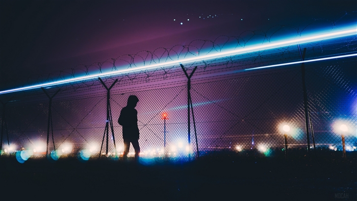 Silhouette of a man by a barbed wire fence at night