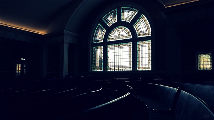 Stained glass window in a dark auditorium with benches