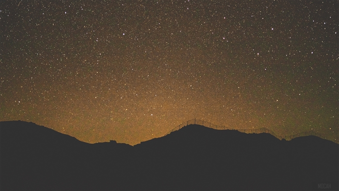 Starry night sky over mountains with fence