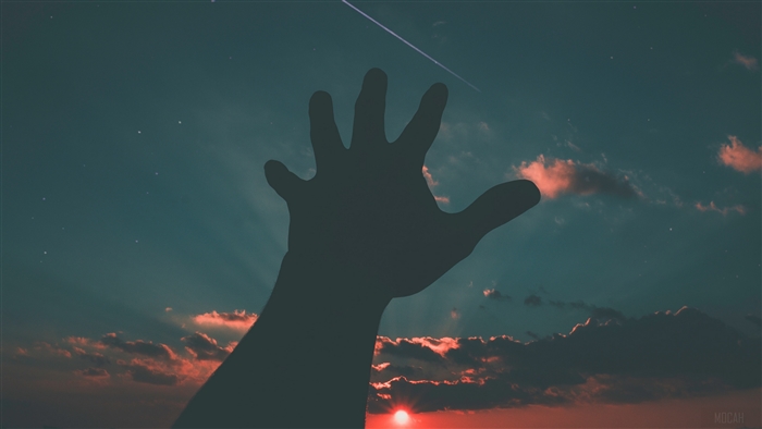 Silhouette of a hand reaching towards a starry sky with a sunset