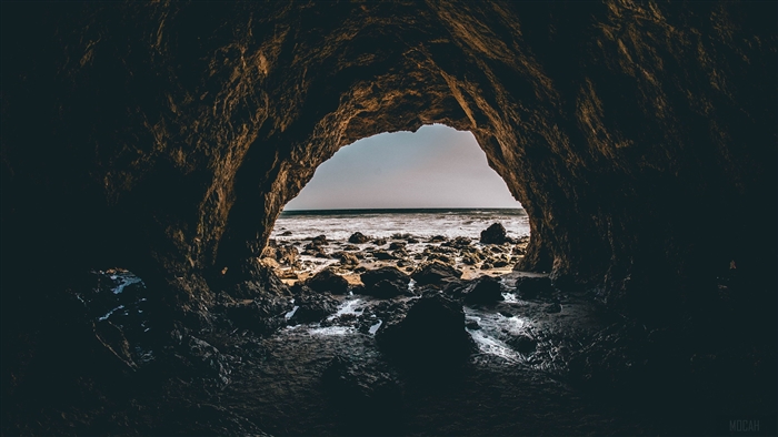 Cave entrance overlooking the ocean and rocky shore 4K