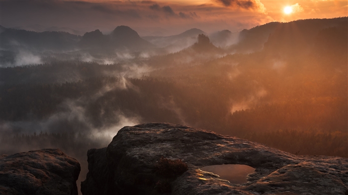 Rock formation overlooking misty forest at sunset