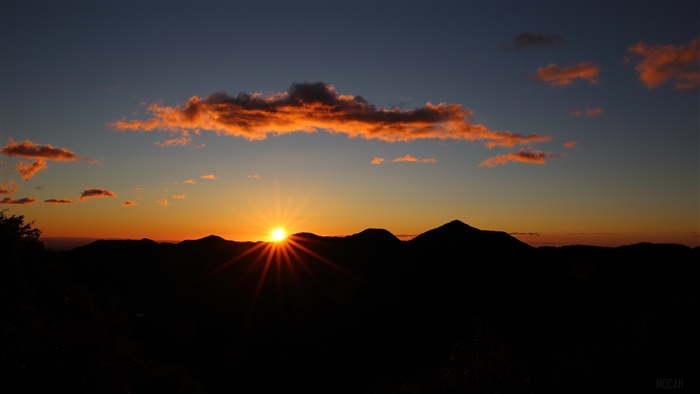 Sunset over silhouetted hills with orange clouds
