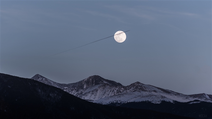Moon and Airplane Trail Over Snowy Mountains