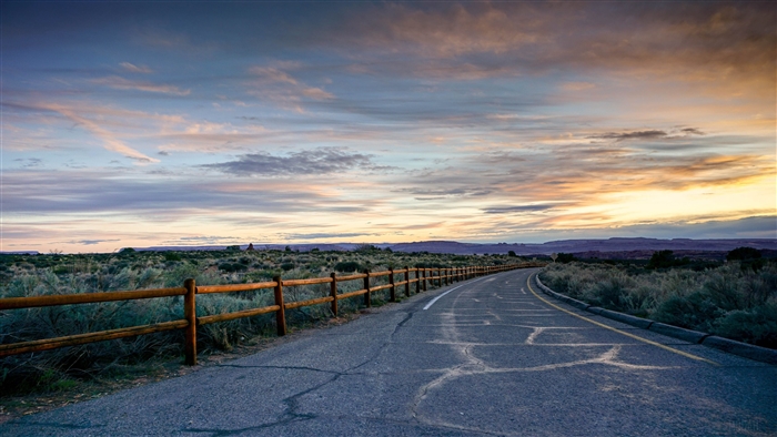 Sunset over a desert road with a wooden fence