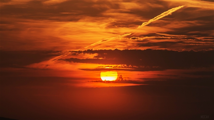 Sunset behind clouds with contrail