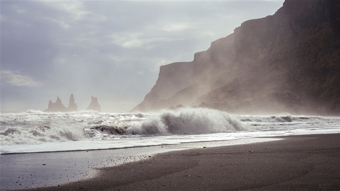 Waves crashing on a black sand beach with sea stacks