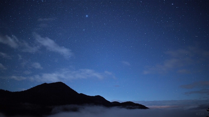 Night sky with stars and clouds over mountains