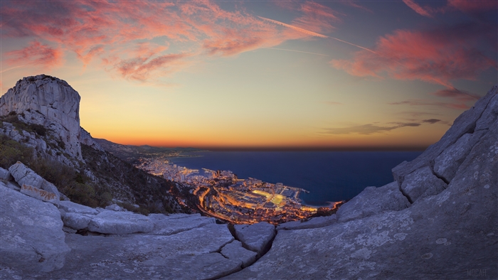 City lights by the sea at sunset from a rocky viewpoint
