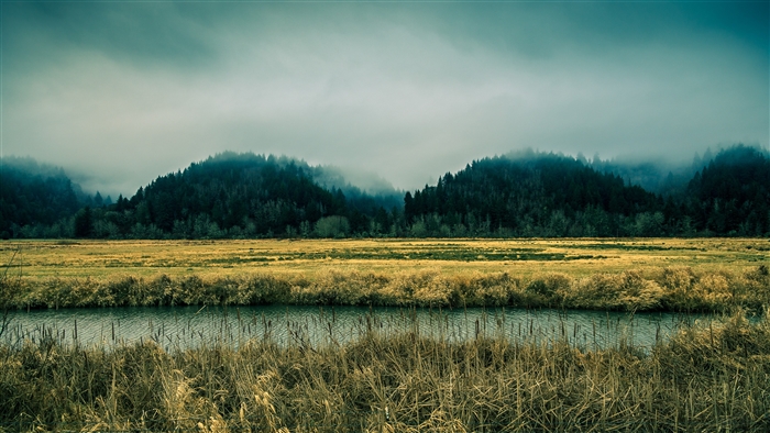 Mountains shrouded in fog over a field and river