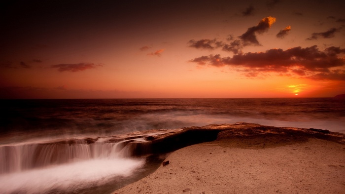 Sunset over the ocean with rocky shore