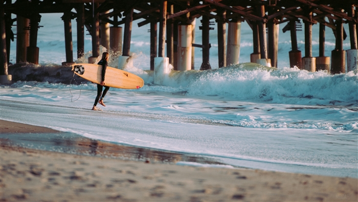 Surfer with surfboard walking near pier and waves 4K