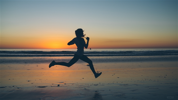 Silhouette of a woman running on the beach at sunset 4K
