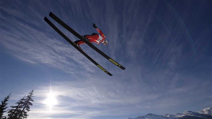 Skier jumping in the sky with mountains and sun