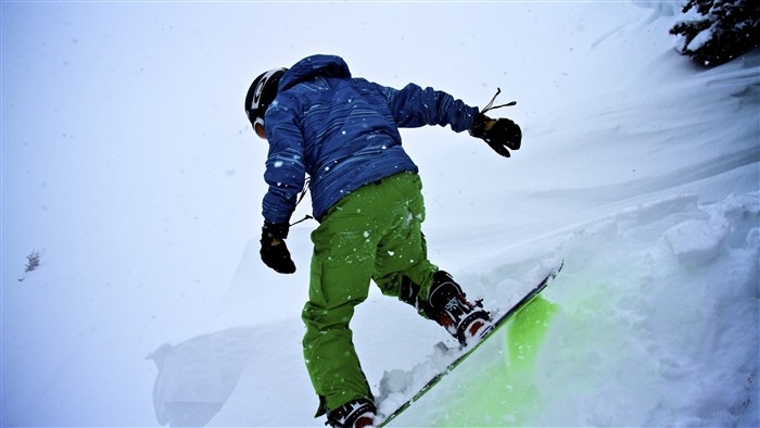 Snowboarder in blue jacket and green pants during snowfall