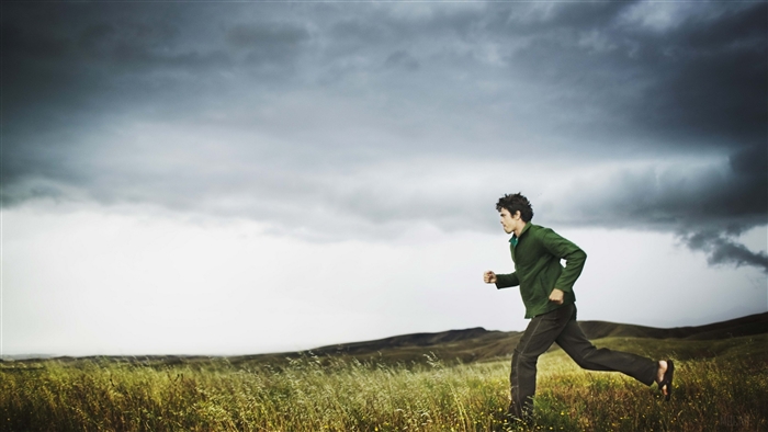 Man running in a field under stormy clouds 4K