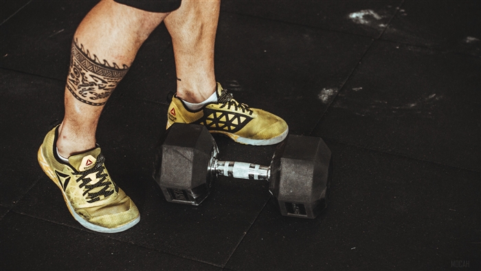 Man's legs with tattoo and Reebok shoes on dumbbell
