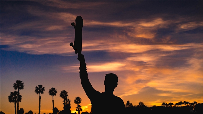 Silhouette of a person holding a skateboard at sunset