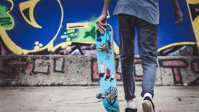 Skateboarder holding skateboard in front of graffiti wall 4K