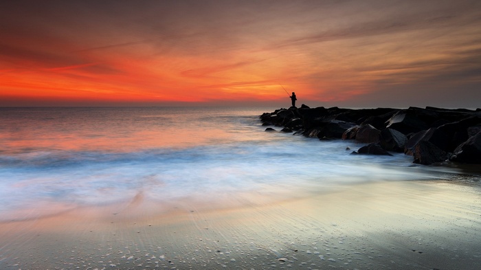 Fisherman on rocks at sunset over the ocean