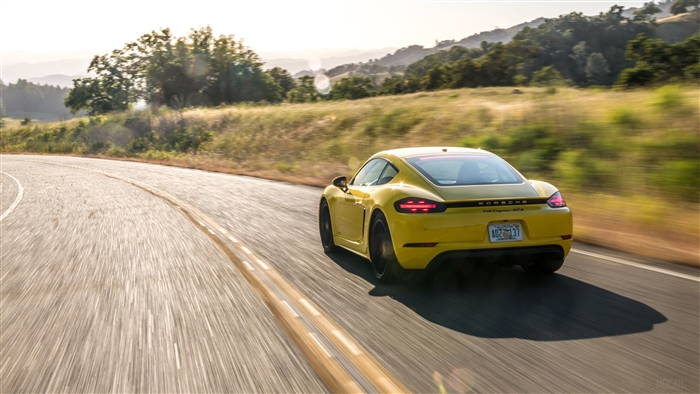 Yellow Porsche 718 Cayman GTS driving on a winding road