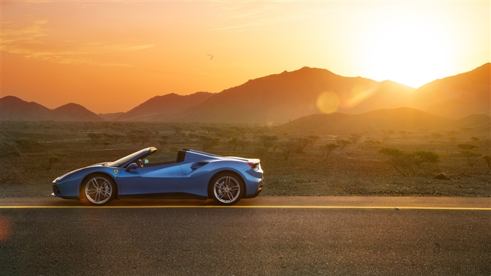 Blue Ferrari 488 Spyder convertible on a road at sunset