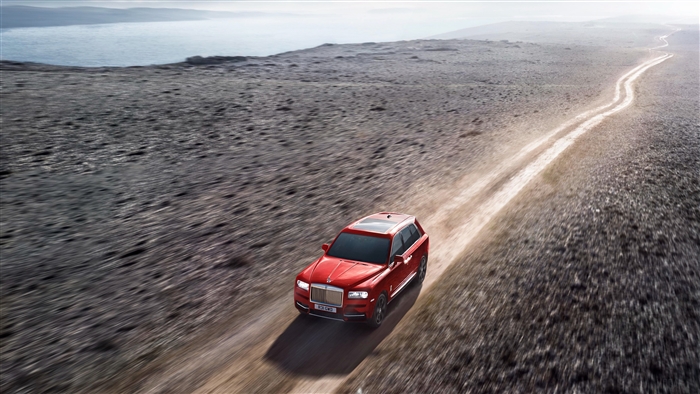 Red Rolls Royce Cullinan driving on dirt road