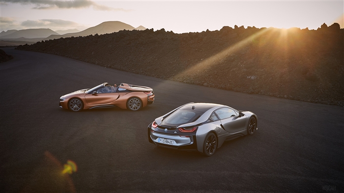 Two BMW i8 cars on a road at sunset