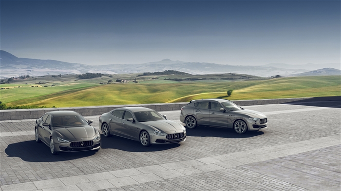 Three Maseratis parked in front of rolling hills
