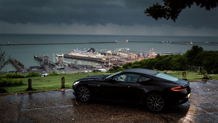Black Aston Martin DB11 parked by the sea in the rain