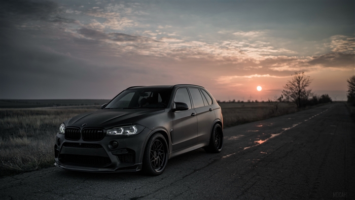 Matte black BMW X5 M on a road at sunset