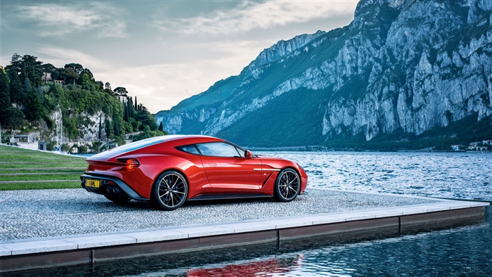 Red Aston Martin Vanquish parked by a lake with mountains