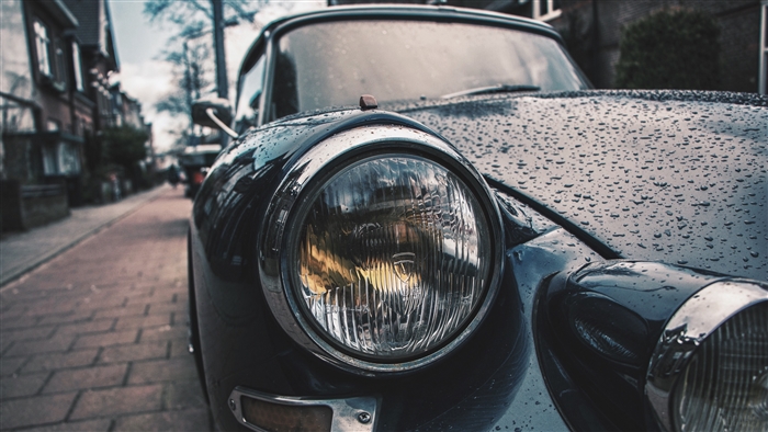 Close-up of a vintage car headlight with raindrops