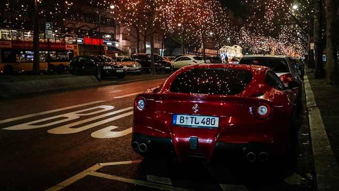 Red Ferrari F12 Berlinetta parked at night with city lights