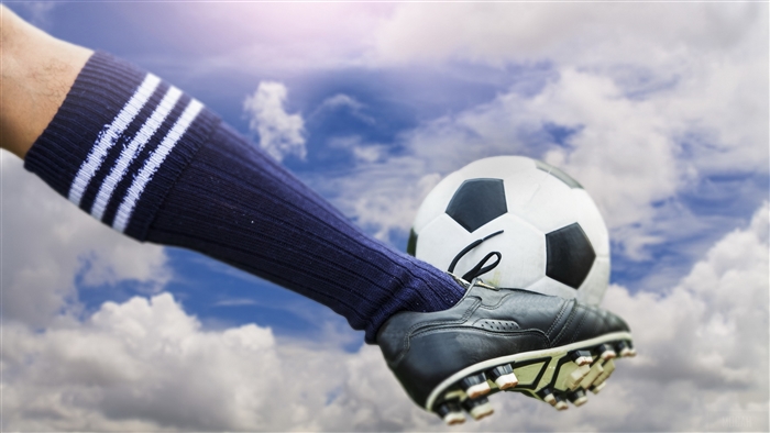 Football boot kicking a soccer ball against cloudy sky