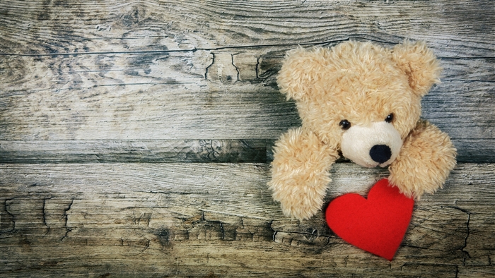 Teddy bear holding a red heart on wooden background 4K