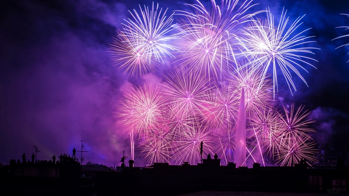 Fireworks display over a city skyline with people watching